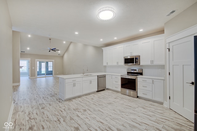 kitchen with lofted ceiling, sink, kitchen peninsula, white cabinetry, and stainless steel appliances