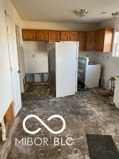 kitchen featuring brown cabinetry, freestanding refrigerator, and washer / dryer
