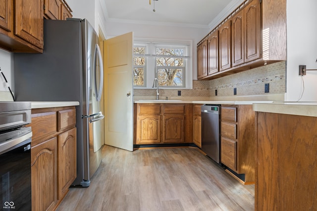 kitchen with appliances with stainless steel finishes, backsplash, ornamental molding, sink, and light hardwood / wood-style flooring