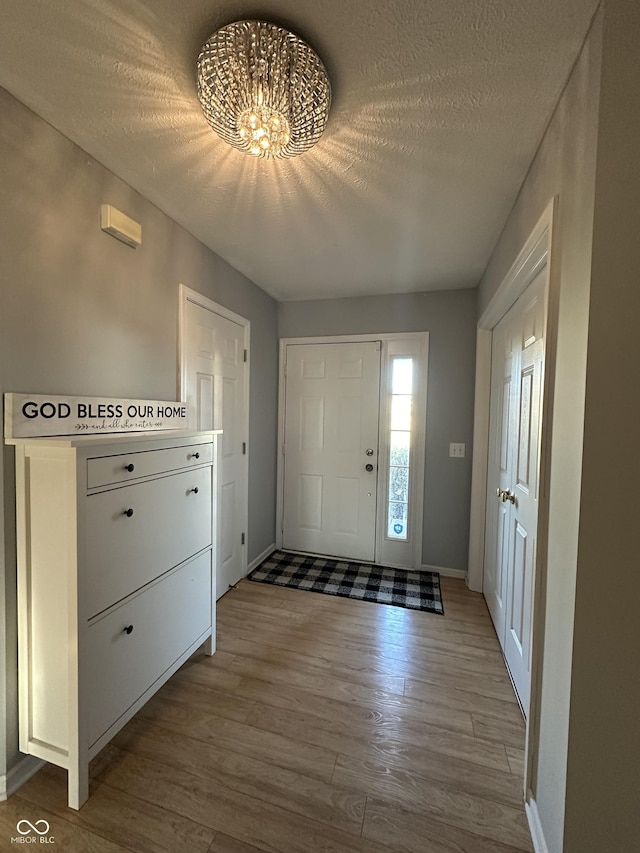 foyer featuring a notable chandelier, a textured ceiling, baseboards, and wood finished floors