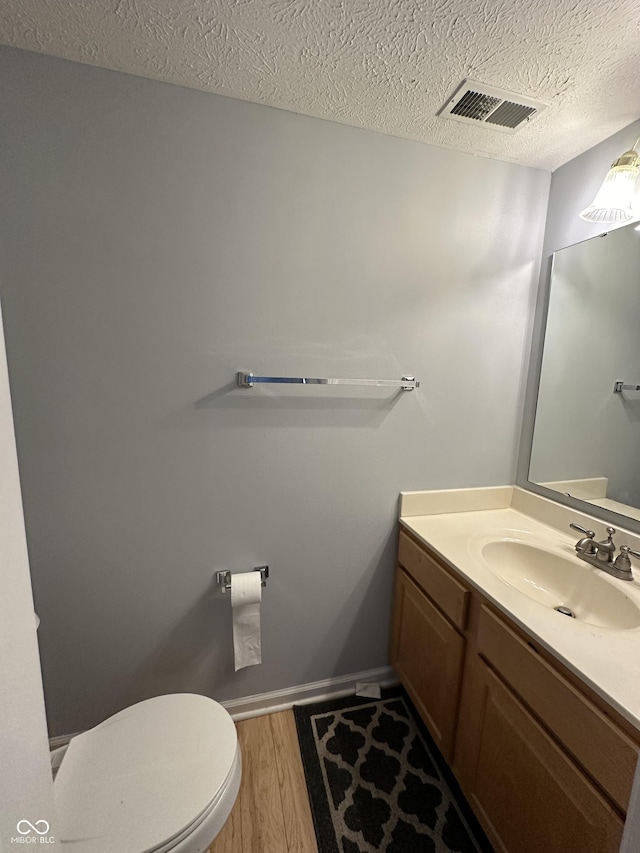 half bathroom with visible vents, toilet, a textured ceiling, wood finished floors, and vanity