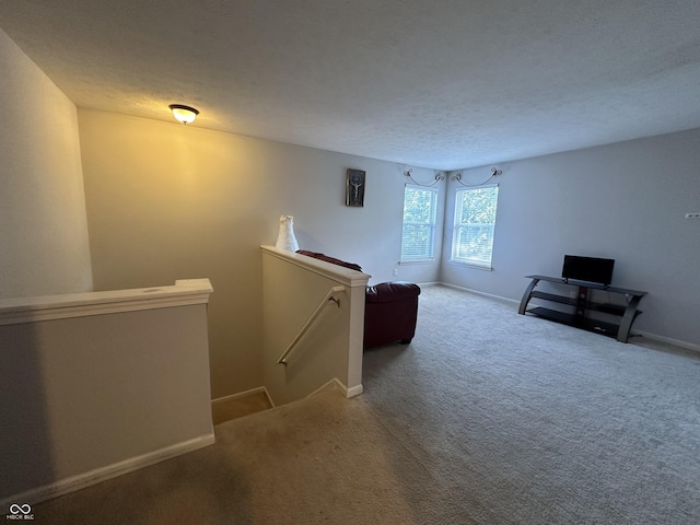 unfurnished room featuring an upstairs landing, a textured ceiling, baseboards, and carpet floors