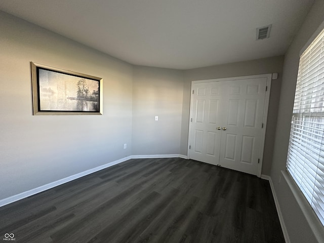 unfurnished bedroom with dark wood finished floors, visible vents, baseboards, and a closet