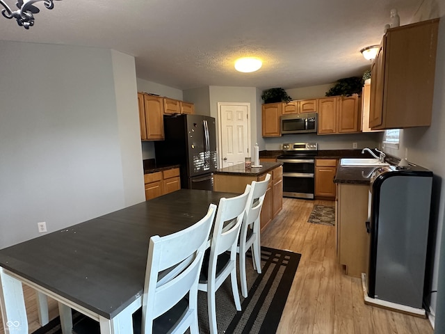 kitchen with dark countertops, a kitchen island, light wood-style floors, stainless steel appliances, and a sink