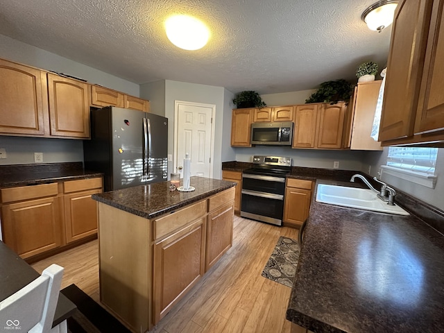 kitchen with light wood finished floors, a kitchen island, stainless steel appliances, and a sink