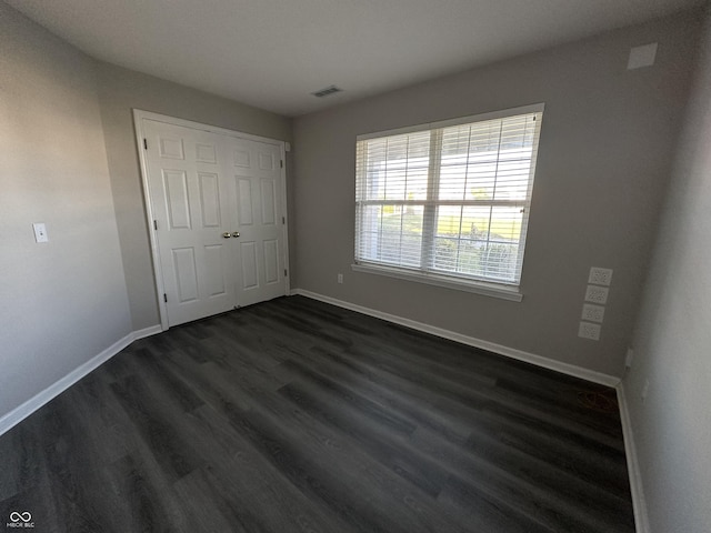 unfurnished bedroom featuring dark wood-type flooring, baseboards, visible vents, and a closet