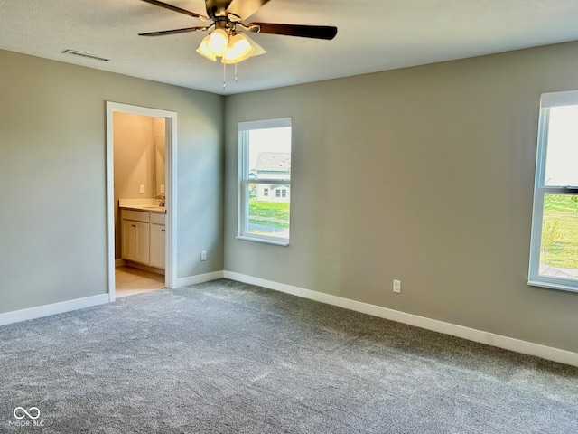 unfurnished bedroom featuring multiple windows, ceiling fan, light colored carpet, and connected bathroom