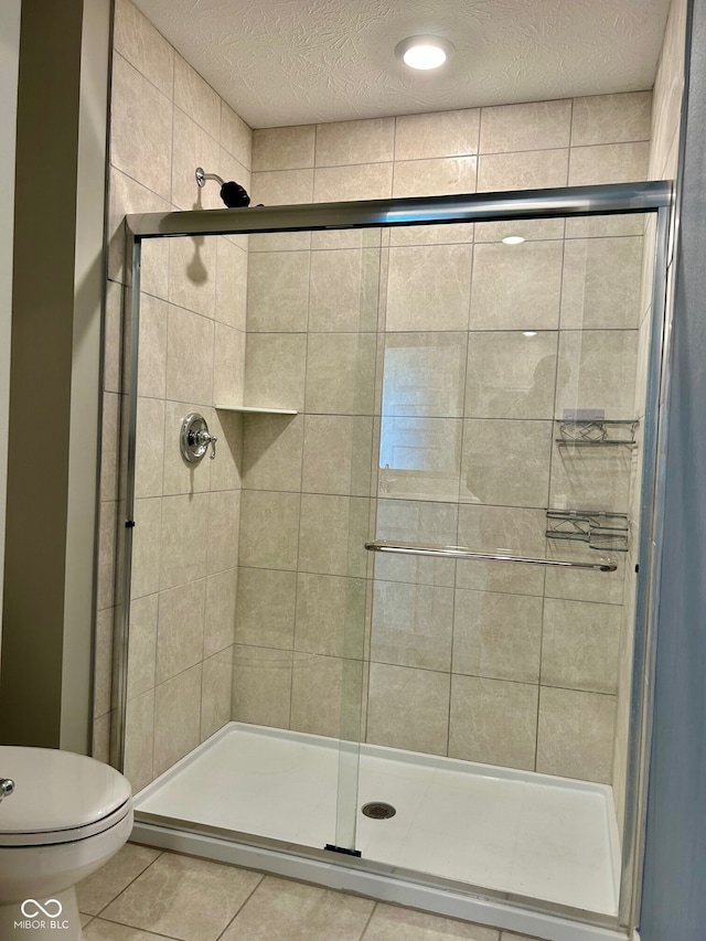 bathroom featuring a textured ceiling, a shower with shower door, toilet, and tile patterned floors