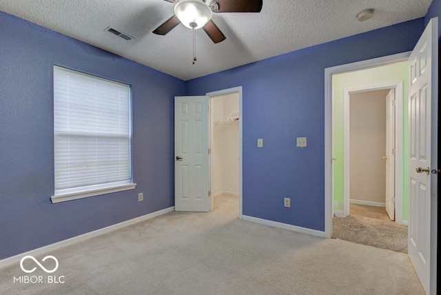 unfurnished bedroom with light carpet, a closet, a spacious closet, and ceiling fan