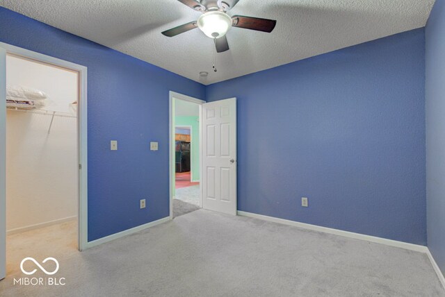 unfurnished bedroom featuring light carpet, a textured ceiling, ceiling fan, a spacious closet, and a closet