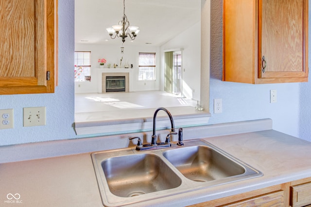 kitchen with pendant lighting, sink, vaulted ceiling, a fireplace, and a notable chandelier