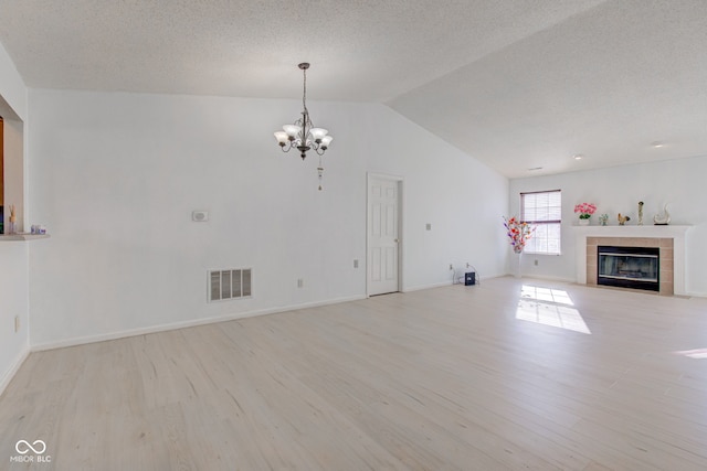 unfurnished living room featuring lofted ceiling, light wood-type flooring, a tile fireplace, and a chandelier