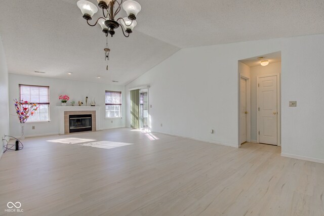 unfurnished living room featuring vaulted ceiling, a textured ceiling, a fireplace, light hardwood / wood-style floors, and a chandelier