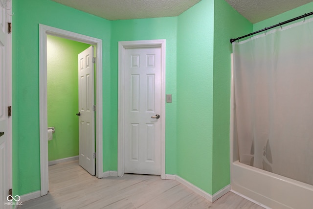 bathroom with wood-type flooring, shower / bathtub combination with curtain, and a textured ceiling