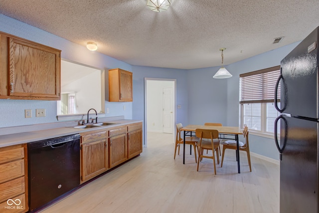 kitchen with a textured ceiling, sink, black appliances, decorative light fixtures, and light hardwood / wood-style floors