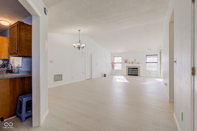 unfurnished living room with an inviting chandelier, light hardwood / wood-style floors, a textured ceiling, and vaulted ceiling