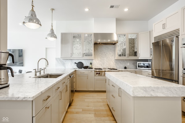 kitchen with a kitchen island, light hardwood / wood-style flooring, stainless steel appliances, sink, and wall chimney range hood