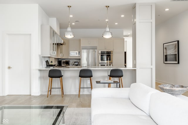 kitchen with built in appliances, a kitchen breakfast bar, decorative light fixtures, backsplash, and light wood-type flooring