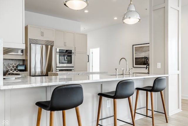 kitchen with a breakfast bar, stainless steel appliances, kitchen peninsula, and light hardwood / wood-style floors