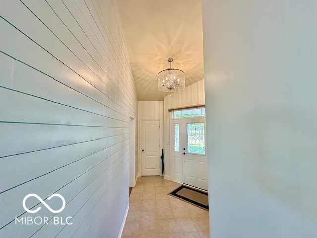 entryway with wood walls, an inviting chandelier, and light tile patterned flooring