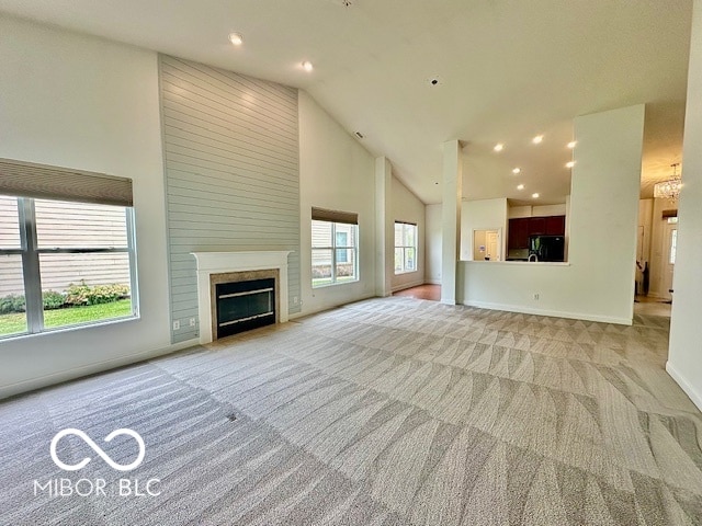 unfurnished living room with a healthy amount of sunlight, a high end fireplace, light carpet, and high vaulted ceiling