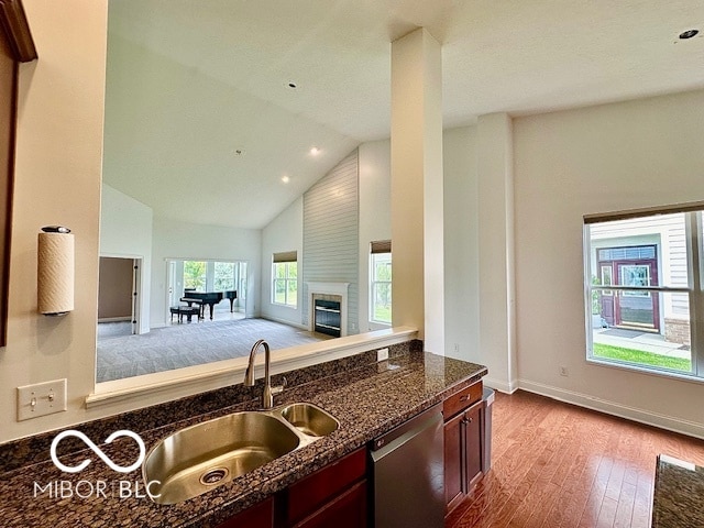 kitchen with dishwasher, light hardwood / wood-style floors, sink, high vaulted ceiling, and dark stone counters