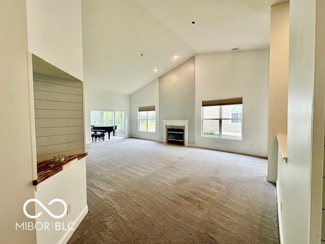 unfurnished living room featuring a large fireplace, high vaulted ceiling, and light colored carpet