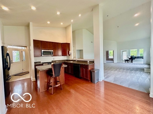 kitchen featuring light hardwood / wood-style floors, sink, black appliances, dark stone counters, and high vaulted ceiling