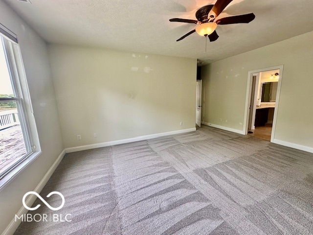 unfurnished bedroom featuring light carpet, a textured ceiling, connected bathroom, and ceiling fan