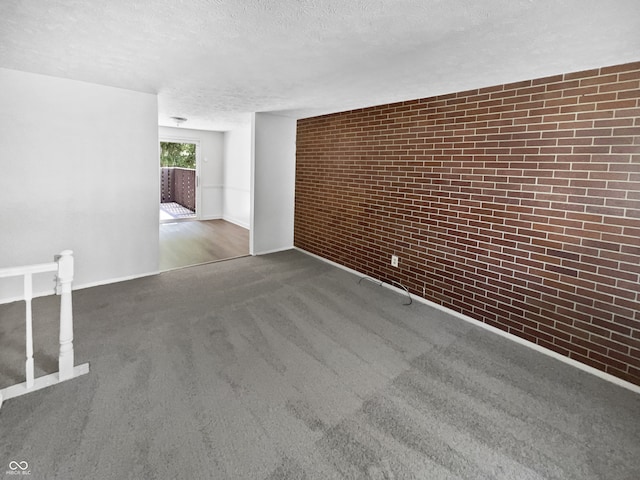 unfurnished room featuring a textured ceiling, brick wall, and carpet floors