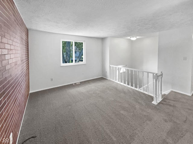 carpeted spare room featuring a textured ceiling and brick wall