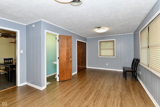 interior space featuring a textured ceiling, crown molding, wood walls, and hardwood / wood-style floors