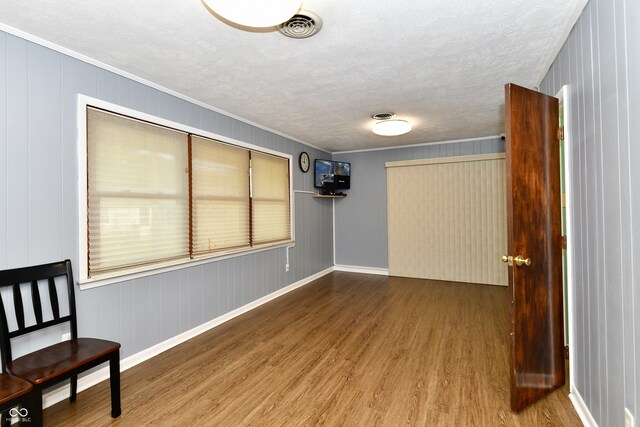 interior space featuring wooden walls, wood-type flooring, ornamental molding, and a textured ceiling