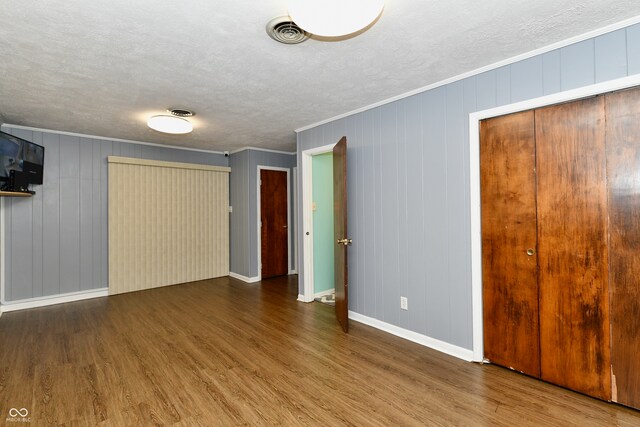 unfurnished bedroom with crown molding, a textured ceiling, wood-type flooring, and wooden walls