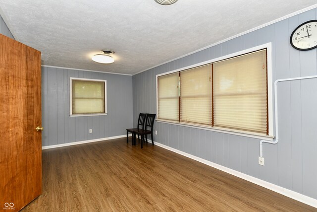 empty room with crown molding, dark hardwood / wood-style flooring, wooden walls, and a textured ceiling