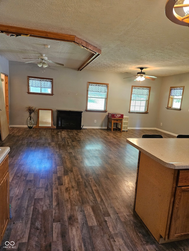 unfurnished living room featuring dark wood-type flooring, ceiling fan, and a textured ceiling