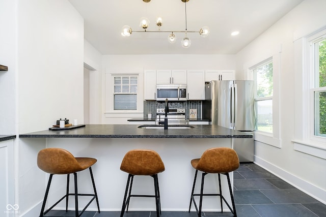 kitchen featuring a kitchen bar, decorative light fixtures, appliances with stainless steel finishes, and white cabinets