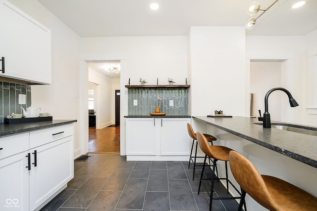 kitchen with a kitchen breakfast bar, backsplash, sink, a chandelier, and white cabinets