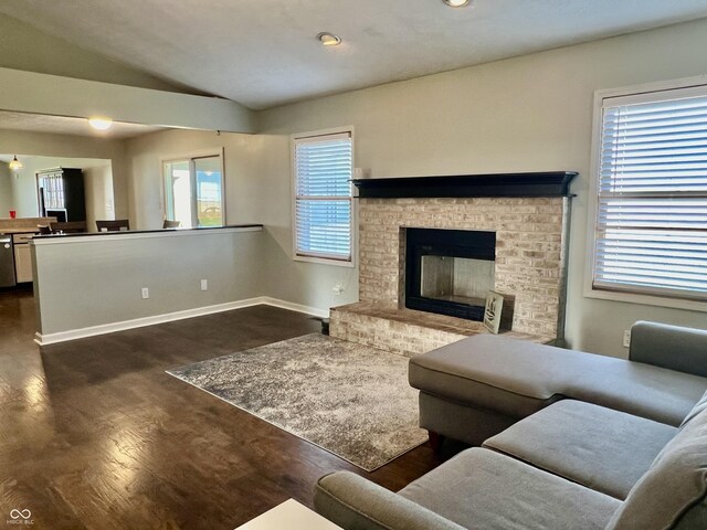 living room with a wealth of natural light, dark hardwood / wood-style flooring, vaulted ceiling, and a brick fireplace