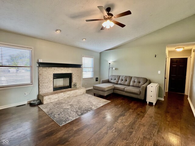 living room with a brick fireplace, a textured ceiling, vaulted ceiling, ceiling fan, and dark hardwood / wood-style floors