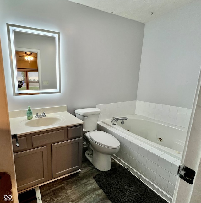 bathroom featuring ceiling fan, a relaxing tiled tub, wood-type flooring, toilet, and vanity