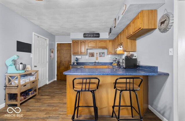 kitchen featuring sink, kitchen peninsula, dark wood-type flooring, a breakfast bar, and a textured ceiling