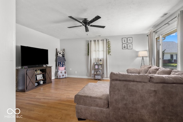 living room with a textured ceiling, ceiling fan, and wood-type flooring