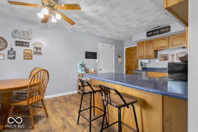 kitchen with dishwasher, kitchen peninsula, ceiling fan, a breakfast bar area, and light hardwood / wood-style floors