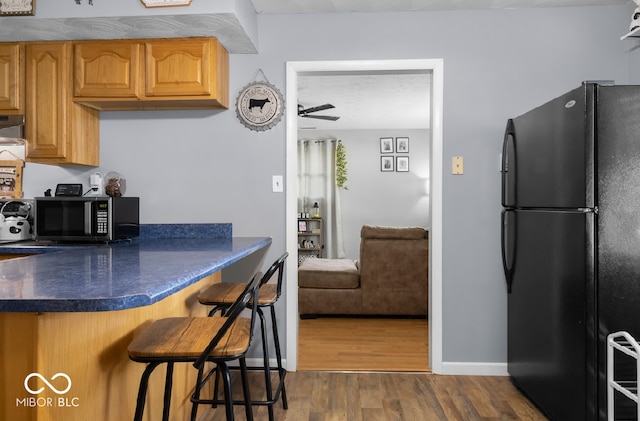 kitchen with a breakfast bar area, dark wood-type flooring, kitchen peninsula, ceiling fan, and black fridge