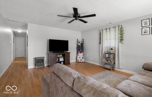 living room with a wood stove, ceiling fan, and light hardwood / wood-style floors