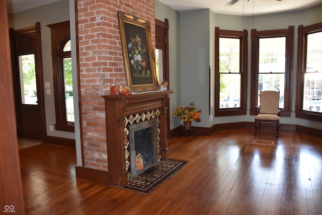 unfurnished living room featuring a brick fireplace, ceiling fan, dark hardwood / wood-style flooring, and a wealth of natural light