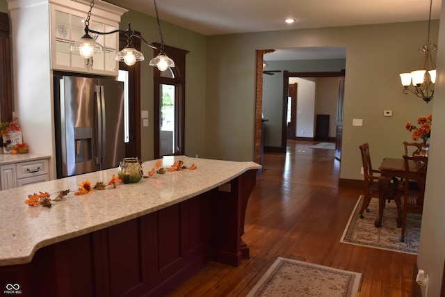 kitchen with light stone counters, dark hardwood / wood-style floors, stainless steel refrigerator with ice dispenser, white cabinetry, and decorative light fixtures