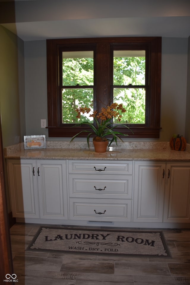 kitchen featuring a healthy amount of sunlight, white cabinetry, light stone counters, and dark wood-type flooring