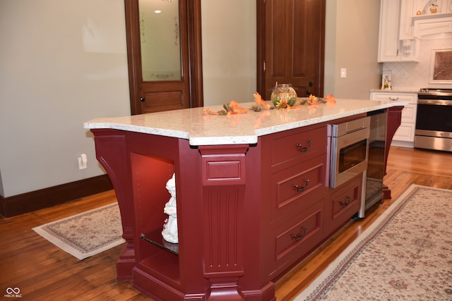 kitchen featuring appliances with stainless steel finishes, light hardwood / wood-style floors, light stone counters, tasteful backsplash, and a center island